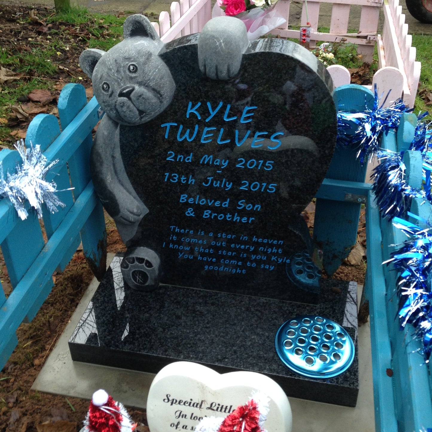 Carved teddy bear on a round top memorial with square base