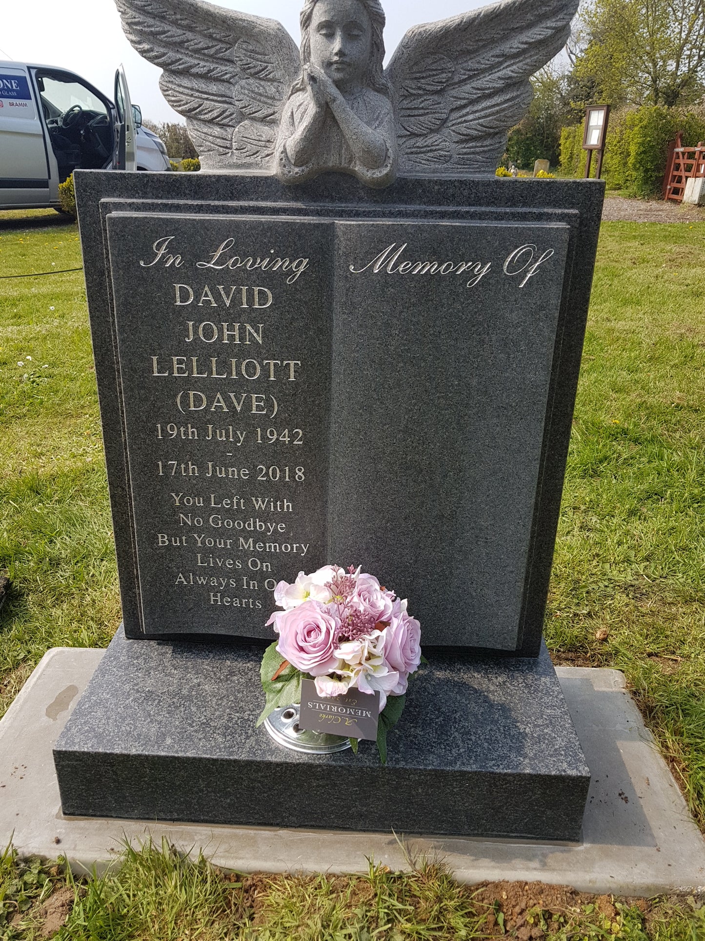 Carved angel resting over a book memorial with a square base