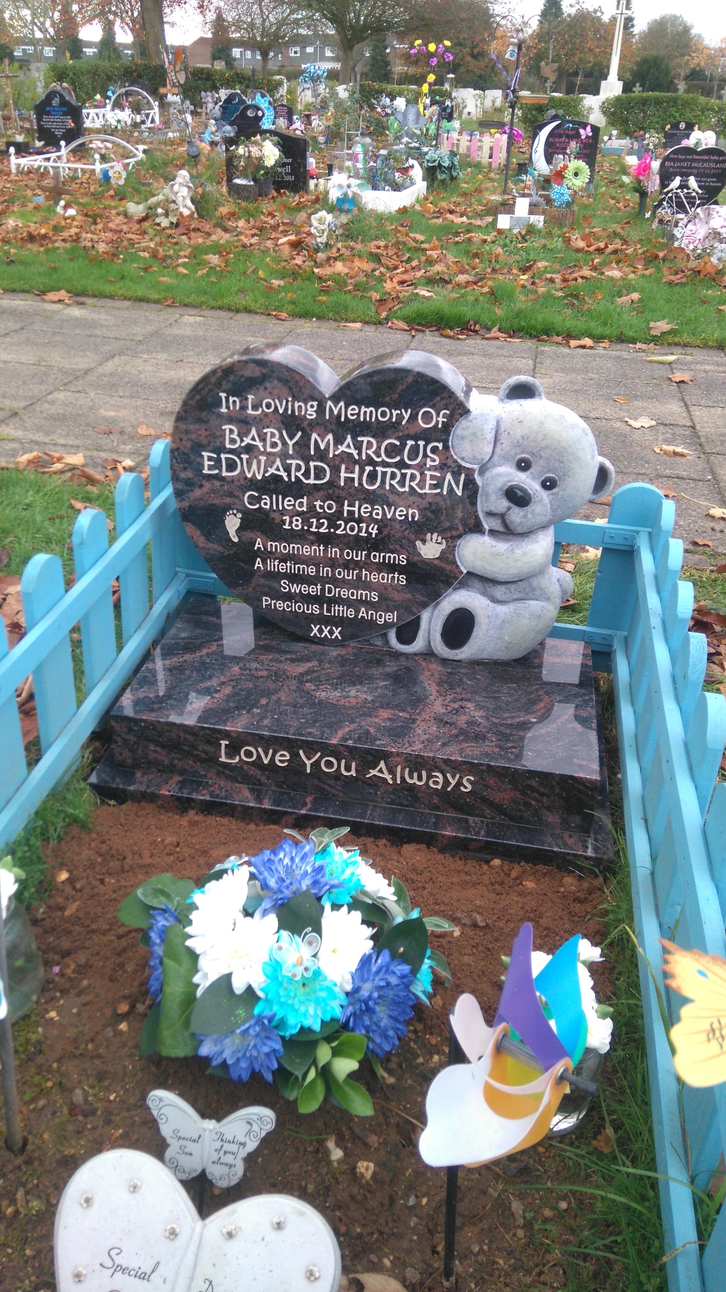 Carved teddy bear holding heart memorial with vase to rear